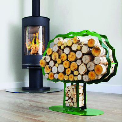 One of Ardour's Oak tree shaped metal log baskets in may-green next to a modern fire. It has a profile of an oak tree with a broad trunk and is attached to a base-plate. The design has two compartments; one in the trunk to store kindling and a large one for the main body of the tree to store the logs.